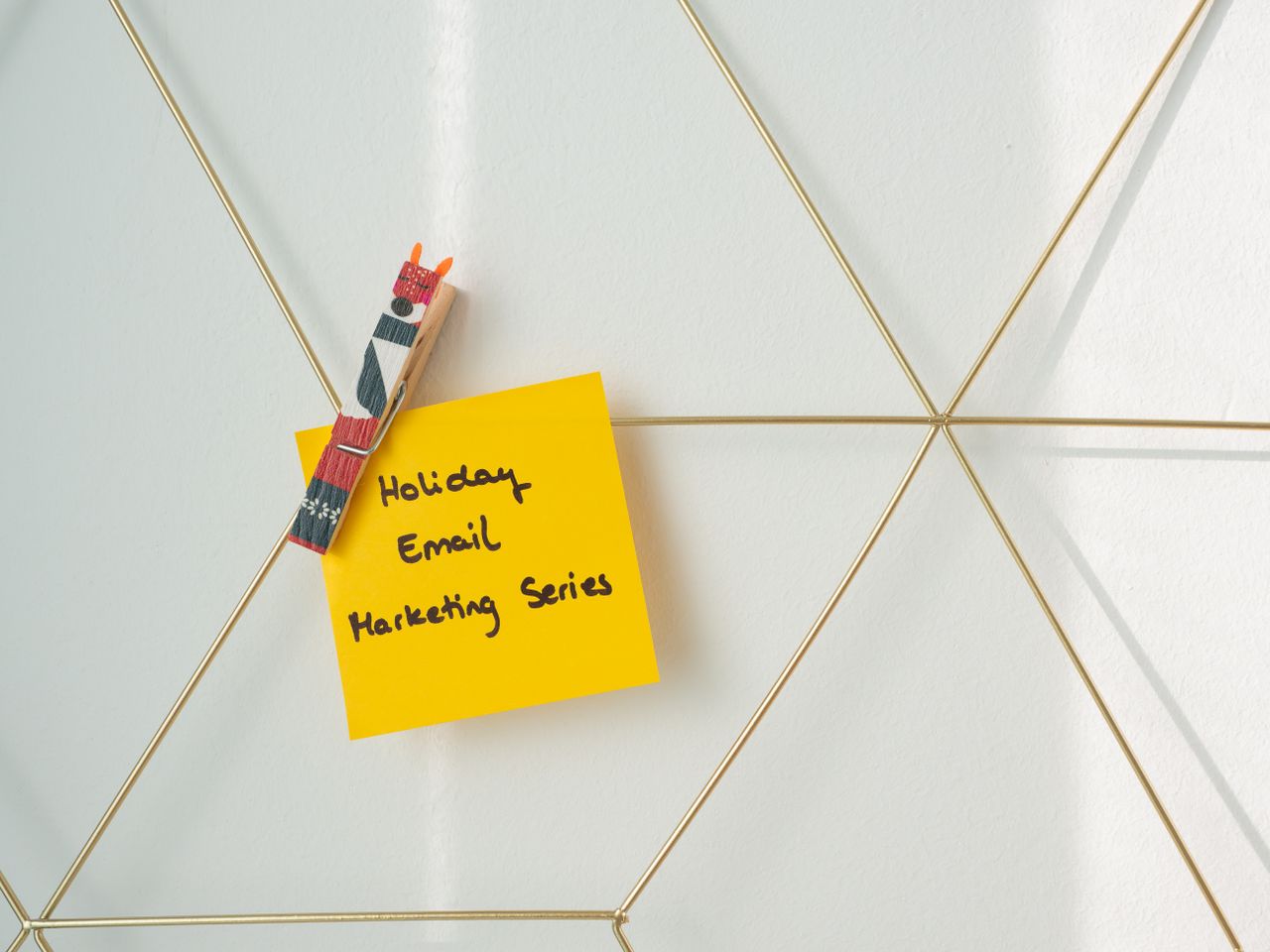 Post-it jaune vif avec un message de marketing par e-mail pour les fêtes, fixé à un mur en fil de fer.